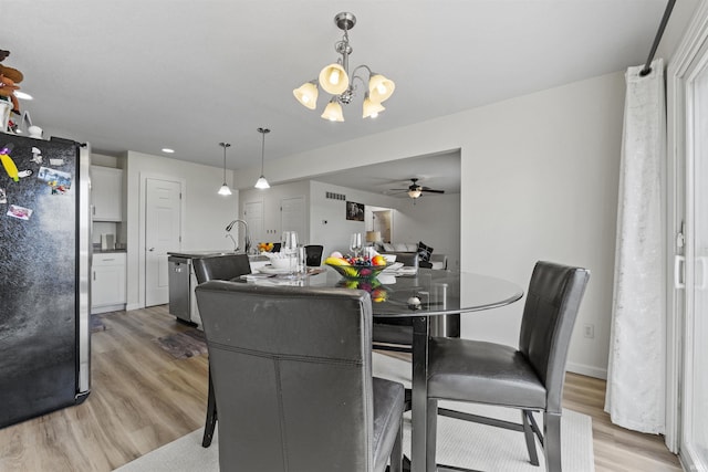 dining space featuring light wood-style flooring, ceiling fan with notable chandelier, and baseboards