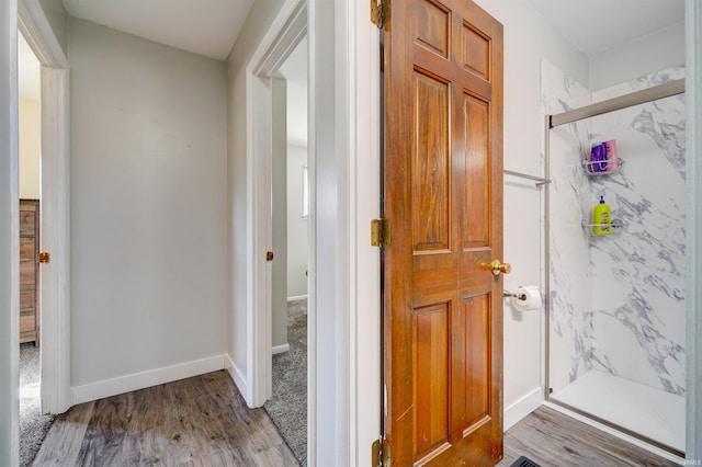 full bath with a marble finish shower, baseboards, and wood finished floors