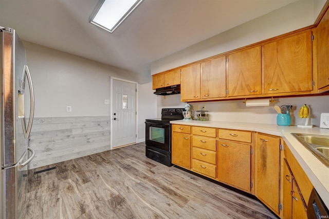 kitchen featuring light wood finished floors, black appliances, under cabinet range hood, a sink, and light countertops