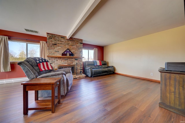 living room featuring visible vents, a brick fireplace, baseboards, beamed ceiling, and wood finished floors