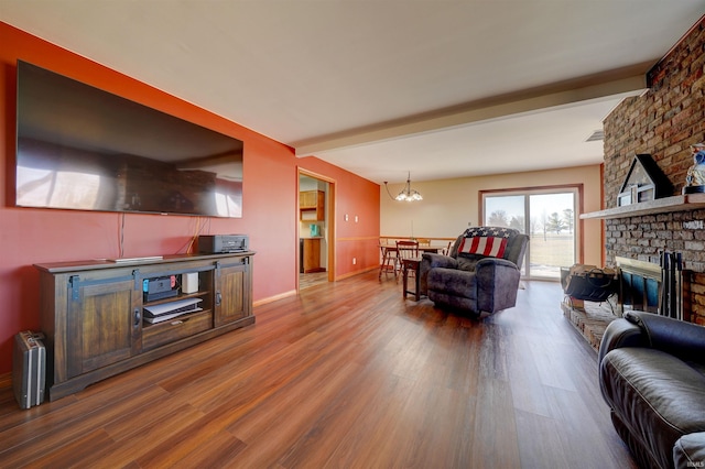 living area with baseboards, beam ceiling, a fireplace, wood finished floors, and a notable chandelier