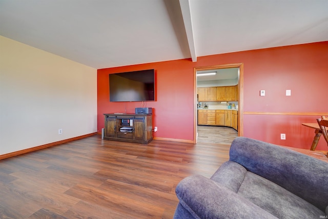 living area with baseboards, beam ceiling, and wood finished floors