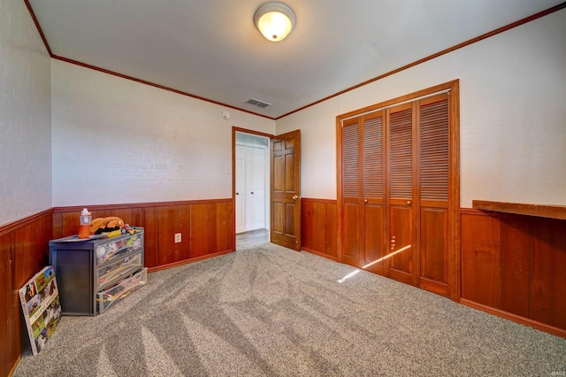 unfurnished bedroom with visible vents, a closet, carpet, wood walls, and wainscoting