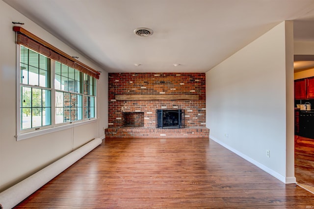 unfurnished living room featuring visible vents, a baseboard heating unit, wood finished floors, baseboards, and a brick fireplace