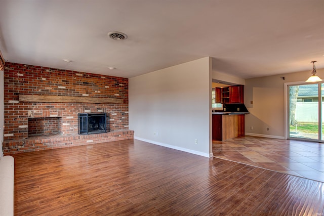 unfurnished living room with a brick fireplace, wood finished floors, visible vents, and baseboards