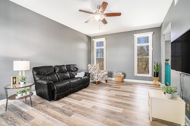 living area featuring light wood-type flooring, baseboards, and a ceiling fan