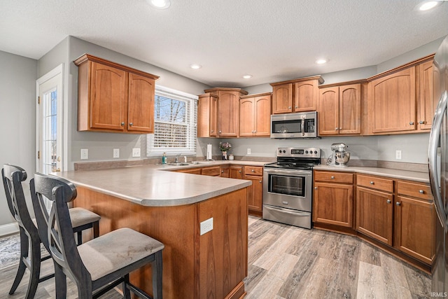 kitchen featuring light wood finished floors, light countertops, a peninsula, a kitchen breakfast bar, and stainless steel appliances