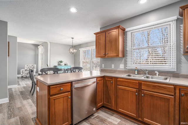 kitchen with stainless steel dishwasher, a peninsula, light countertops, and a sink