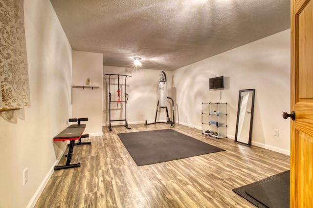 exercise room featuring a textured ceiling, baseboards, and wood finished floors