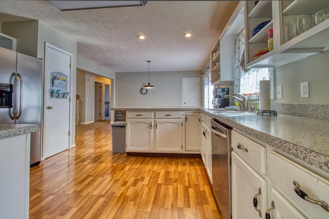 kitchen featuring open shelves, a sink, stainless steel appliances, light wood-style floors, and a textured ceiling