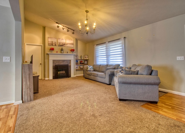 living room with baseboards, vaulted ceiling, a tile fireplace, rail lighting, and a notable chandelier