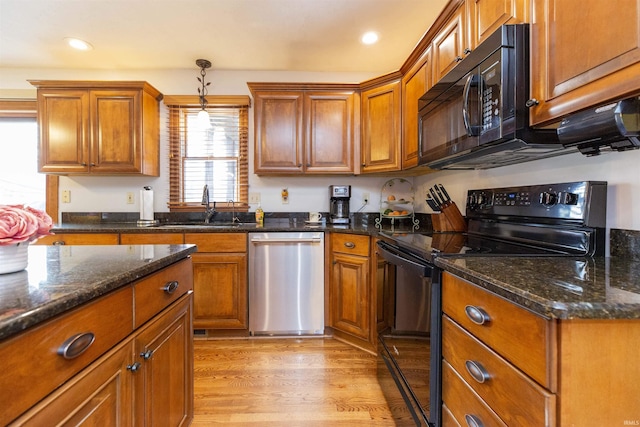 kitchen featuring light wood-style floors, black appliances, brown cabinetry, and hanging light fixtures