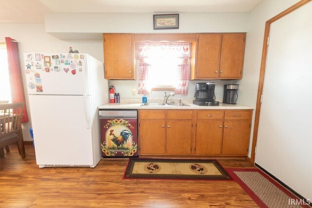 kitchen with dishwashing machine, light wood-style flooring, freestanding refrigerator, a sink, and light countertops