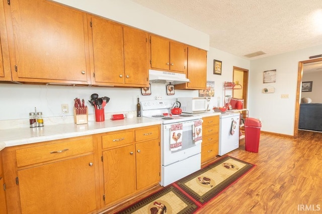 kitchen with light wood finished floors, under cabinet range hood, a textured ceiling, white appliances, and light countertops