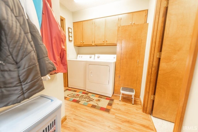 clothes washing area featuring light wood-type flooring, cabinet space, and washer and clothes dryer