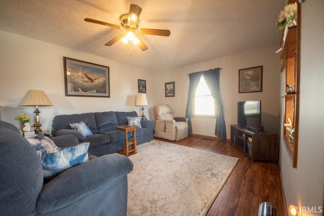 living room featuring dark wood-type flooring, ceiling fan, and a textured ceiling