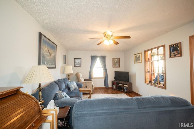 living room with ceiling fan, wood finished floors, baseboards, and a textured ceiling