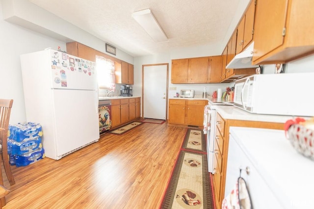 kitchen with white appliances, brown cabinetry, light countertops, and light wood finished floors