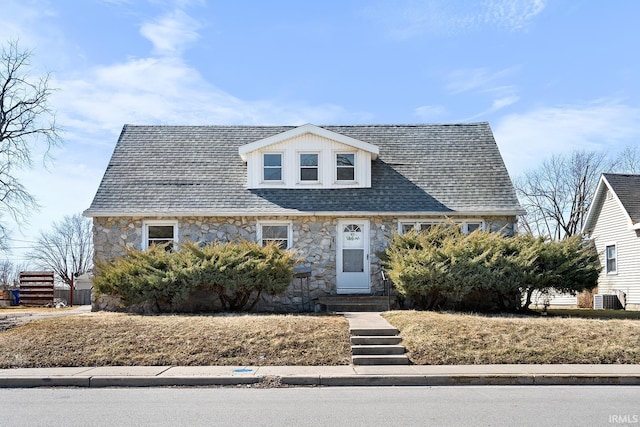 view of front of home with central air condition unit, stone siding, and a shingled roof