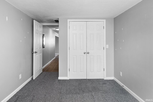 unfurnished bedroom with visible vents, a textured ceiling, a closet, carpet flooring, and baseboards