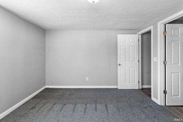 unfurnished room with dark carpet, a textured ceiling, and baseboards