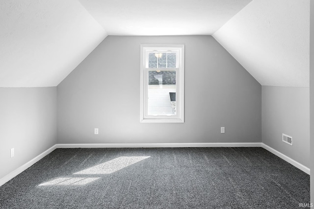 additional living space with visible vents, baseboards, carpet flooring, and vaulted ceiling