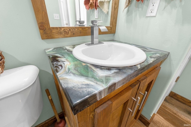 half bath with baseboards, wood finished floors, and vanity