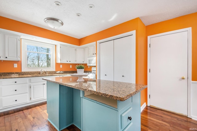 kitchen with wood finished floors, white microwave, a textured ceiling, white cabinetry, and a center island