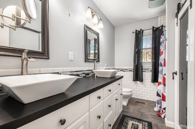 full bath with visible vents, toilet, double vanity, tile walls, and a sink