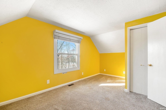 additional living space featuring visible vents, baseboards, carpet floors, vaulted ceiling, and a textured ceiling