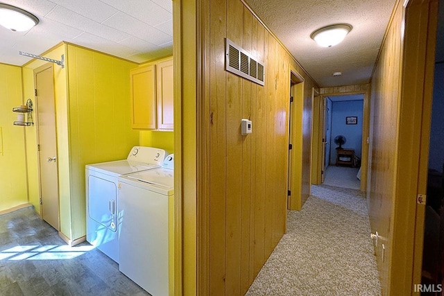 washroom featuring wooden walls, visible vents, cabinet space, a textured ceiling, and washer and clothes dryer