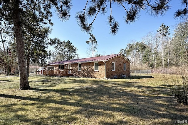 view of property exterior with fence, a yard, a wooden deck, metal roof, and brick siding