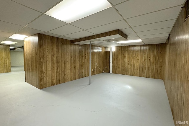 finished basement featuring a paneled ceiling and wood walls