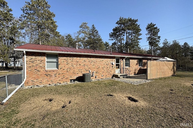 rear view of property featuring fence, a yard, central AC, brick siding, and metal roof