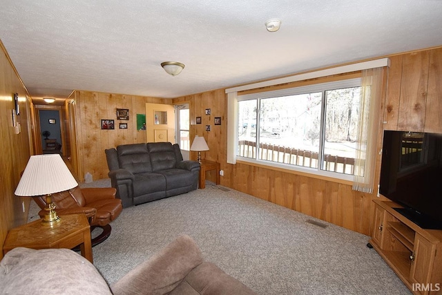 carpeted living area with visible vents, wood walls, and a textured ceiling