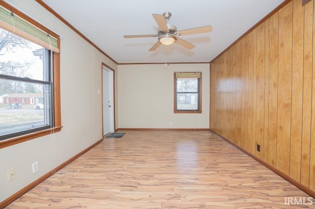 unfurnished room with crown molding, baseboards, wood walls, light wood-type flooring, and a ceiling fan