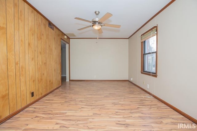 spare room featuring a ceiling fan, light wood-style floors, wood walls, and crown molding