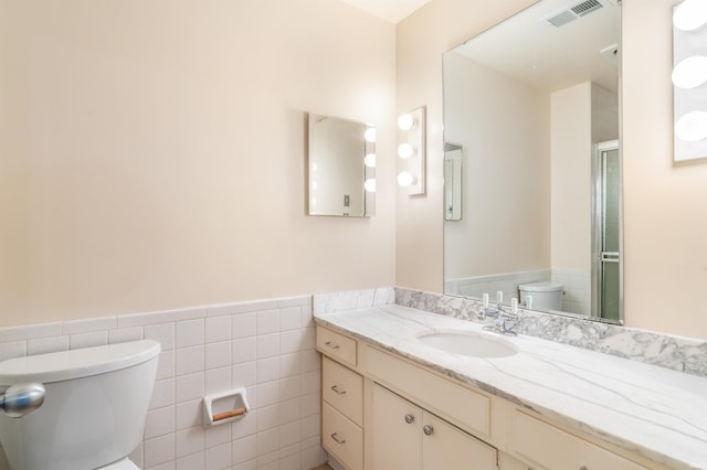 full bathroom with vanity, visible vents, wainscoting, tile walls, and toilet