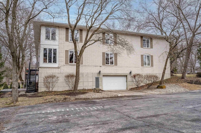 view of side of property with brick siding, driveway, stairs, and a garage