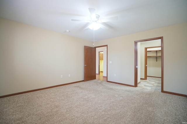 unfurnished bedroom featuring a walk in closet, light colored carpet, baseboards, and ceiling fan