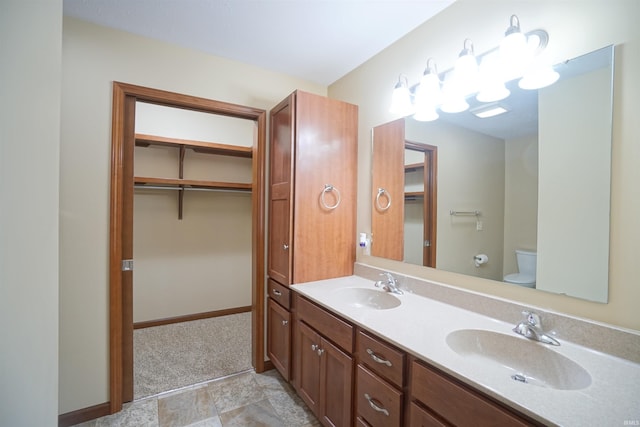 bathroom with double vanity, toilet, baseboards, and a sink