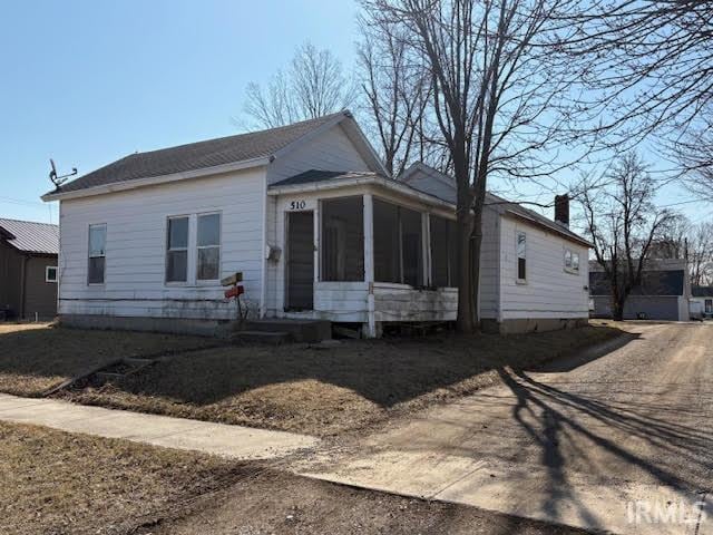 bungalow featuring a chimney, a sunroom, and dirt driveway