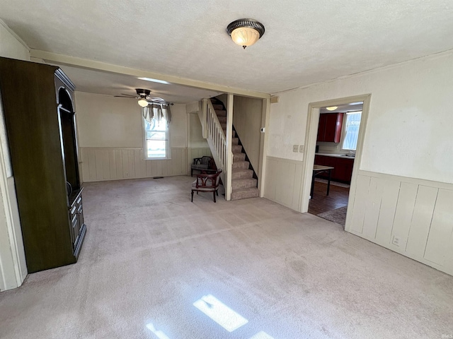 unfurnished room featuring stairs, light colored carpet, a wainscoted wall, and a textured ceiling