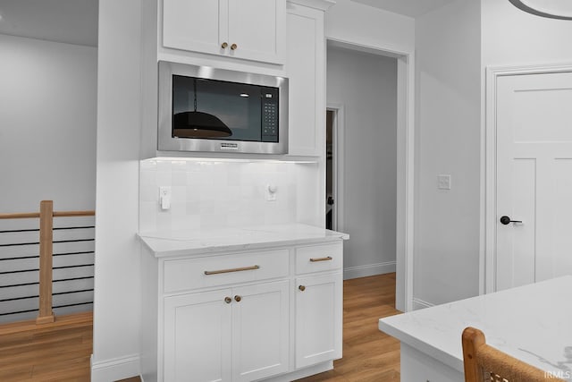 kitchen with white cabinetry, light wood-style flooring, light stone countertops, and built in microwave