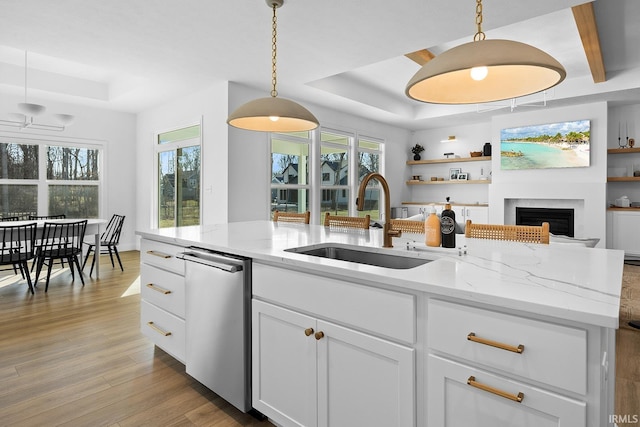 kitchen featuring light wood finished floors, dishwasher, a raised ceiling, and a sink