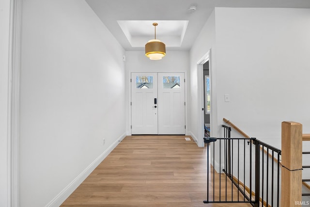 foyer entrance with baseboards, a raised ceiling, and light wood-style floors