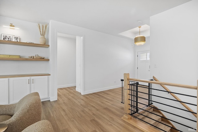 interior space with a raised ceiling, an upstairs landing, baseboards, and light wood finished floors