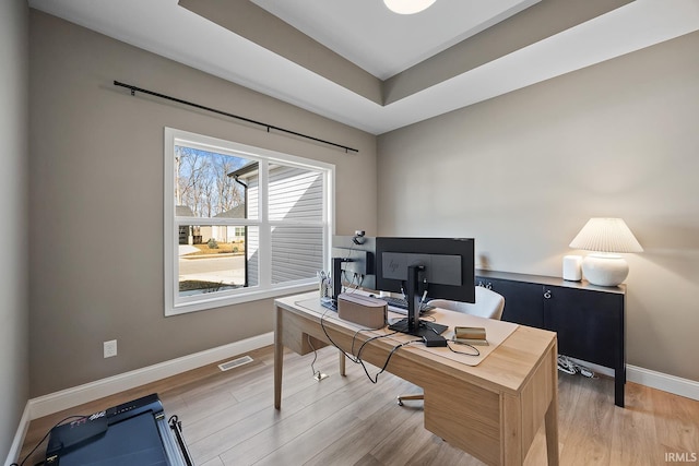 office featuring a tray ceiling, visible vents, baseboards, and light wood finished floors