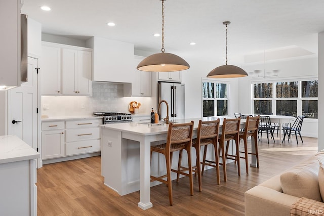 kitchen featuring light wood-style flooring, custom range hood, tasteful backsplash, stainless steel appliances, and white cabinets