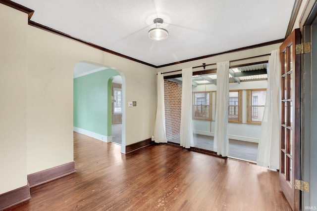 empty room with a healthy amount of sunlight, wood finished floors, arched walkways, and baseboards